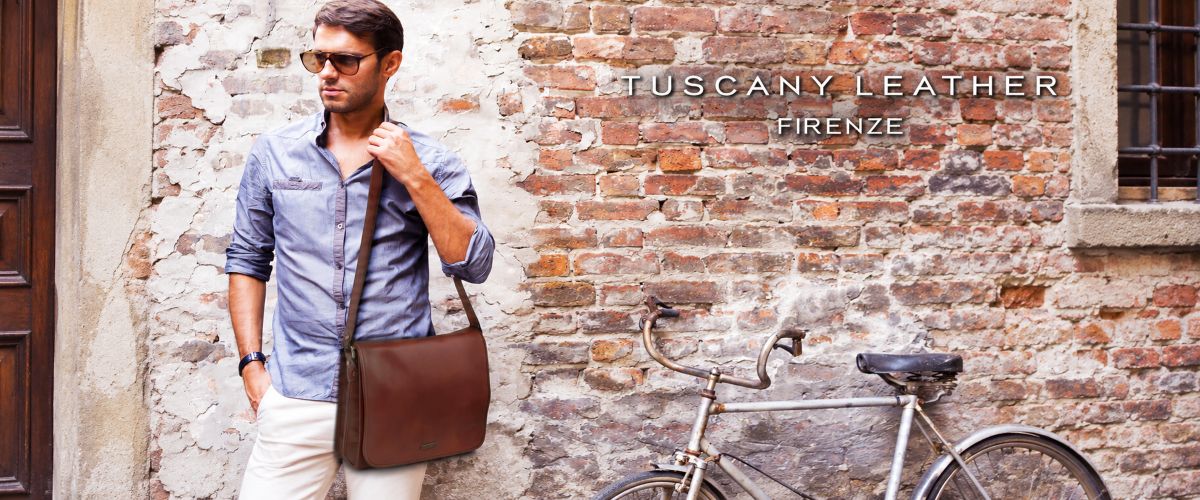 Man carrying a brown leather messenger bag beside a bicycle and brick wall